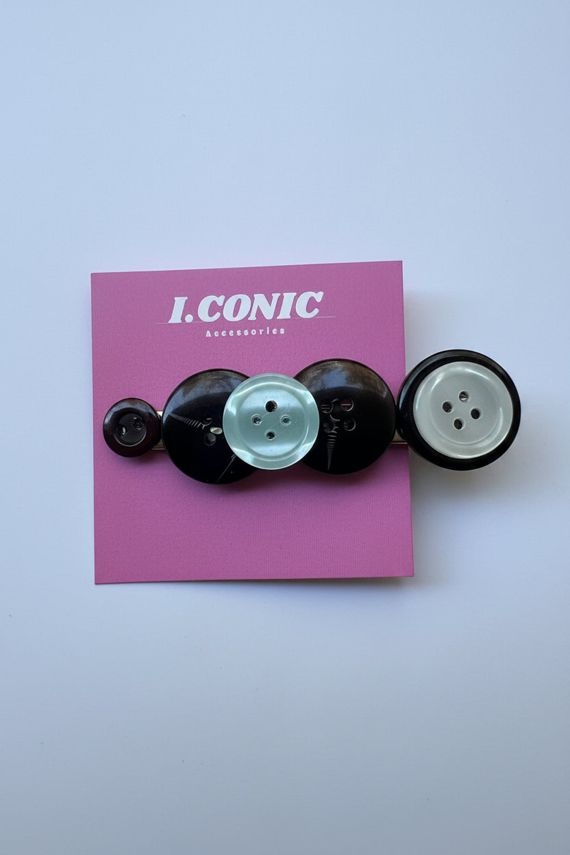 A vertical stack of six decorative buttons in black and pale mint green, mounted on a pink backing card printed with the brand name 'I. CONIC'.